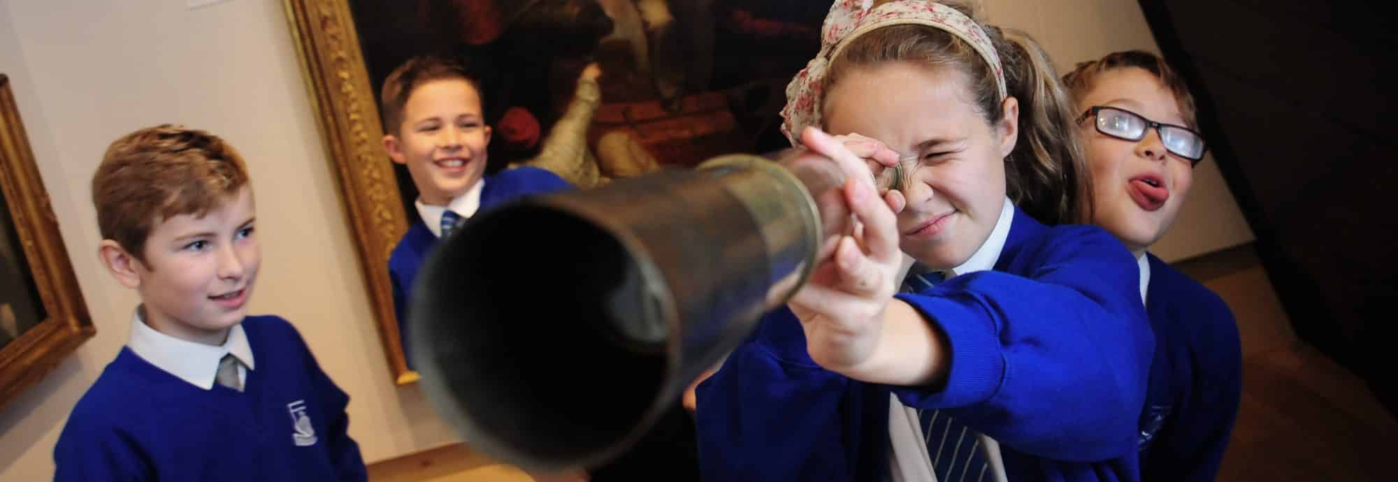A photo of four schoolchildren. One looks at the camera through a telescope.