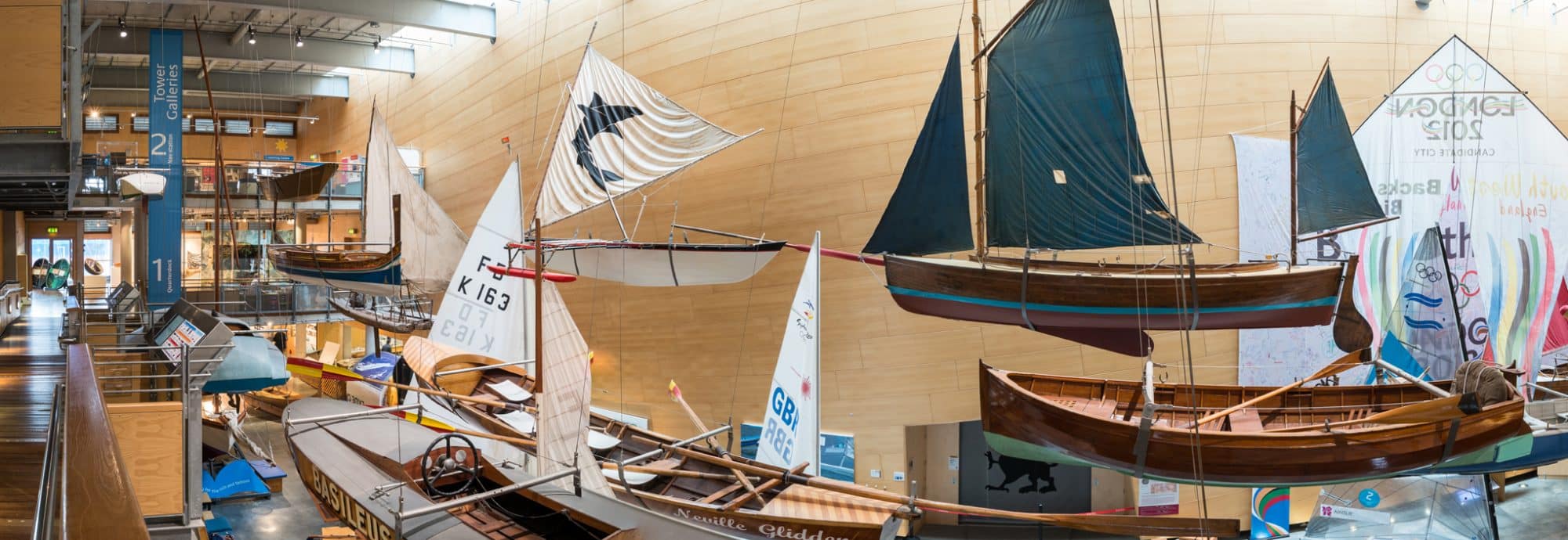 A panorama photo of the flotilla of small boats displayed hanging from the ceiling of the Museum's Main Hall.