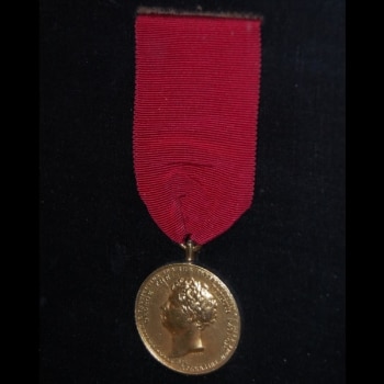 A photo of an RNLI Gold Medal for Gallantry, attached to a red ribbon.