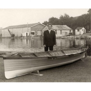 A black and white photo of Vic Angove standing behind a boat.