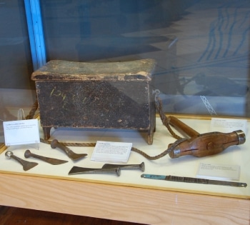 A photo of a wooden box and the tools it would have carried, on display in a cabinet in the Museum.