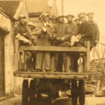 A black and white photo of sailors from 'HMS Cornwall' riding on the back of a truck.