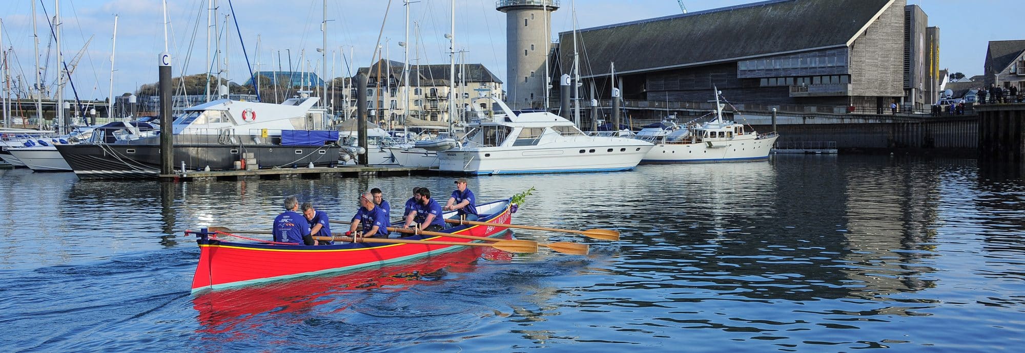 A photo of the 'Valiant' being rowed past Falmouth marina towards the Museum.