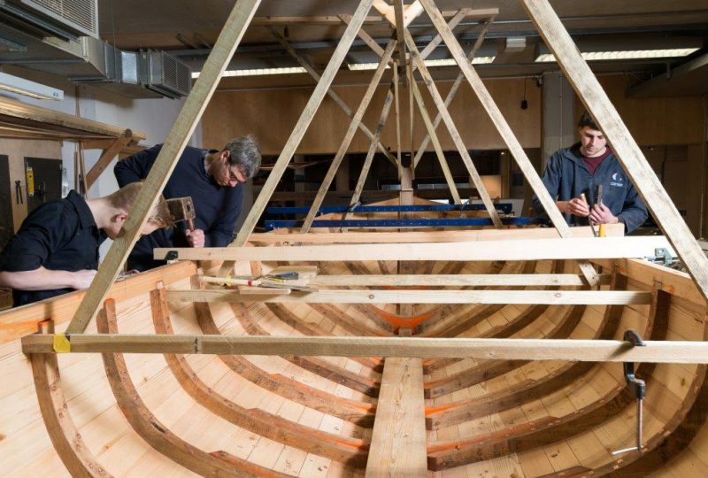 A photo of three volunteers working on a boat in the Museum's boat-building workshop.