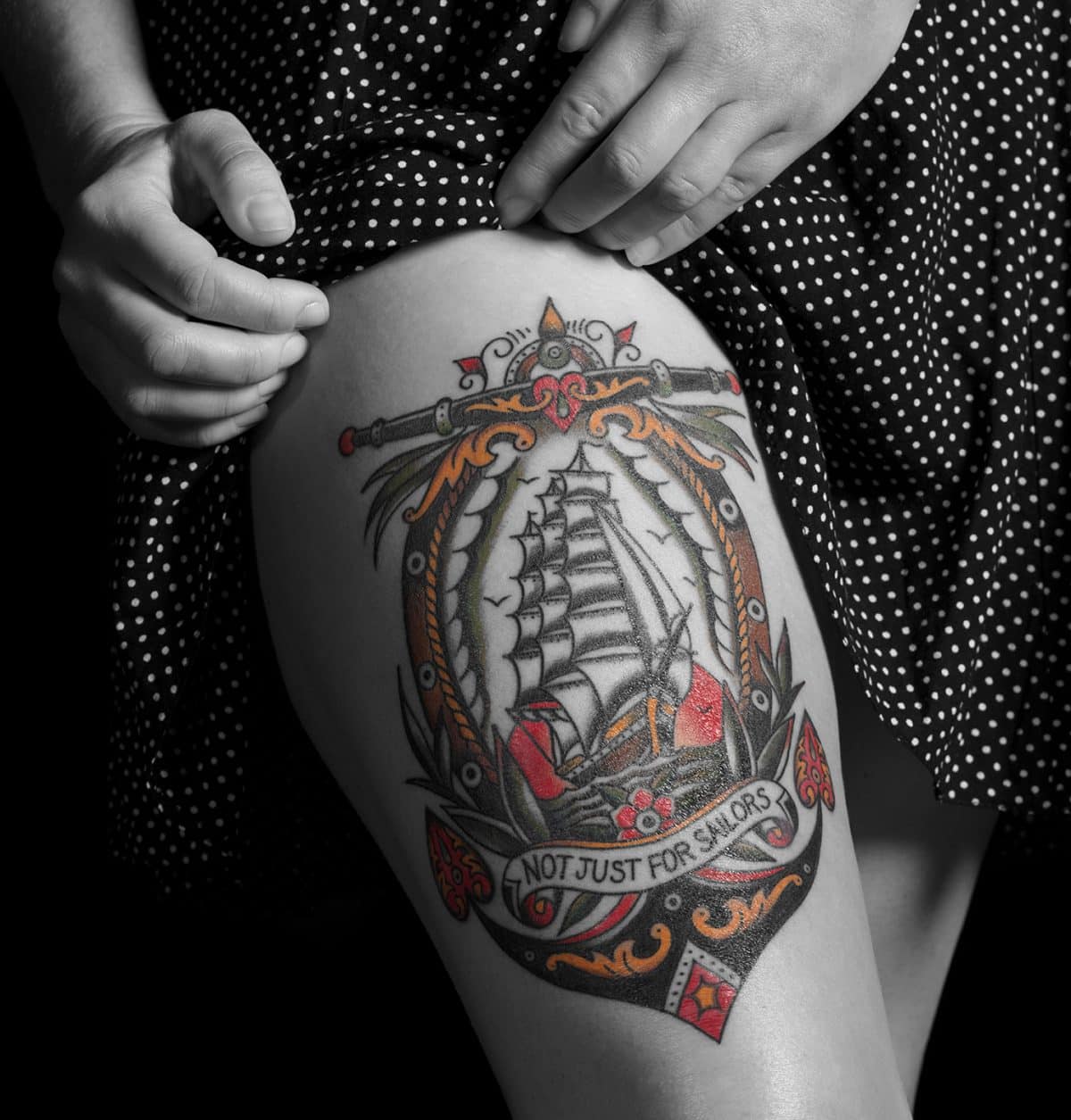 A close-up photo of a tattoo on a woman's thigh. The image is primarily in black and white, except for the small details of the tattoo.