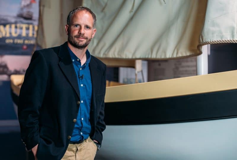 A photo of Conrad Humphreys standing in front of the recreated 'Bounty' launch featured in the Museum's 'Captain Bligh: Myth, Man and Mutiny' exhibition.