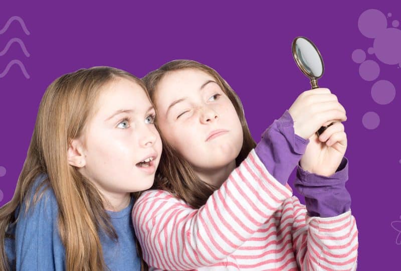 Pictured against a purple background, two girls peer through a magnifying glass.