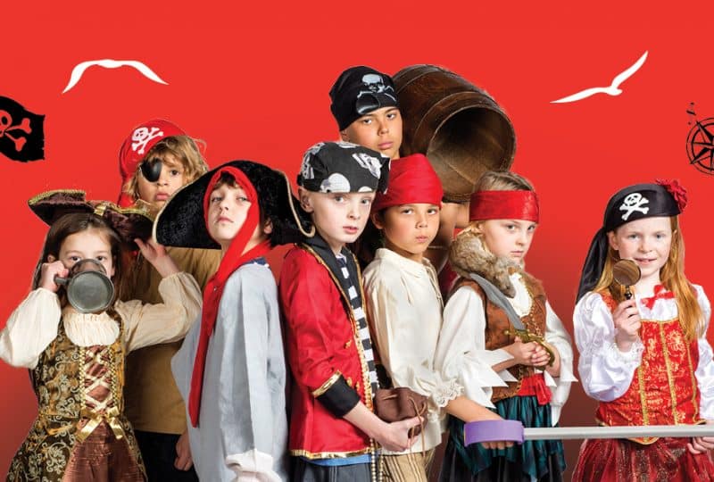 A photo of eight children dressed in pirate costumes, standing against a red background.