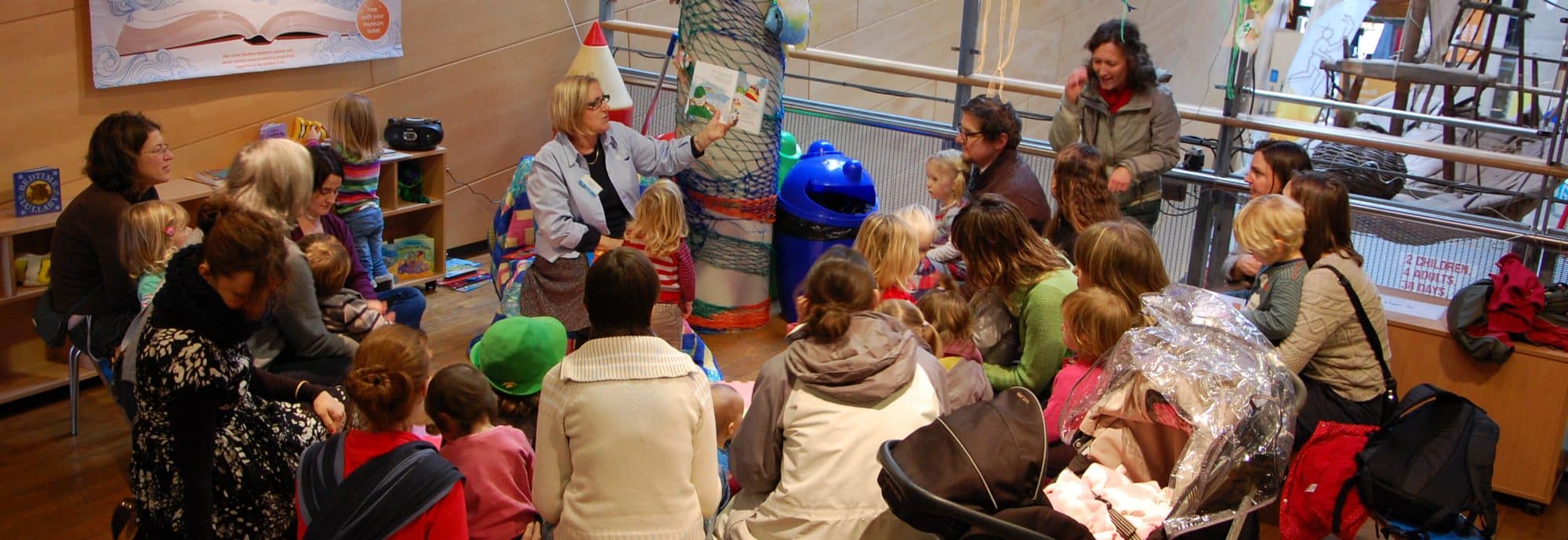 Photo of one of the Museum's Minnows Tales sessions. Young children and their parents sit in a semi-circle around a member of the Museum team.