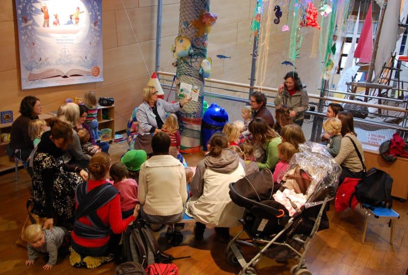 Photo of one of the Museum's Minnows Tales sessions. Young children and their parents sit in a semi-circle around a member of the Museum team.