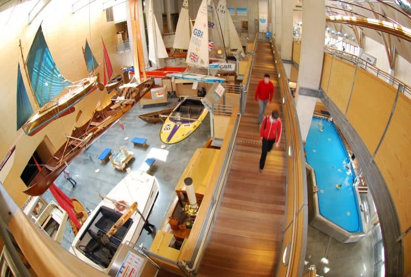 Photo taken from above of two visitors walking down the ramp in the Museum's Main Hall with the flotilla of small boats on the left of the image.