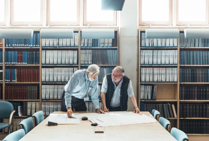 Photo of two volunteers examining diagrams laid out on a table in the Museum's Bartlett Library.