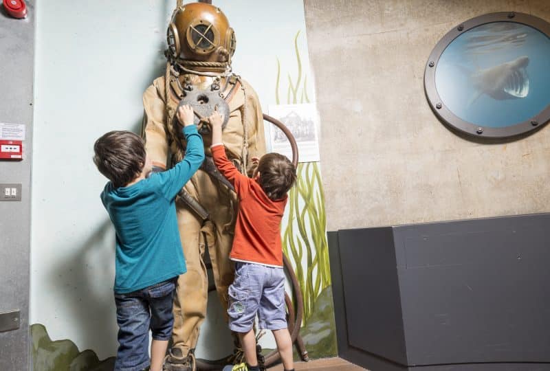 Photo of two young boys standing in front of the diving suit in the Museum's Tidal Zone.