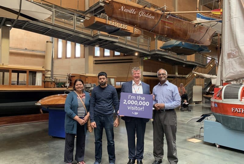 A member of staff holds up a sign saying 'I'm the 2,000,000 visitor!' with three visitors standing beside him.