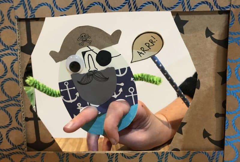A photo of a pirate finger puppet made from card, pipe cleaners and googly eyes. A speech bubble is held up next to it that says 'Arrr!'