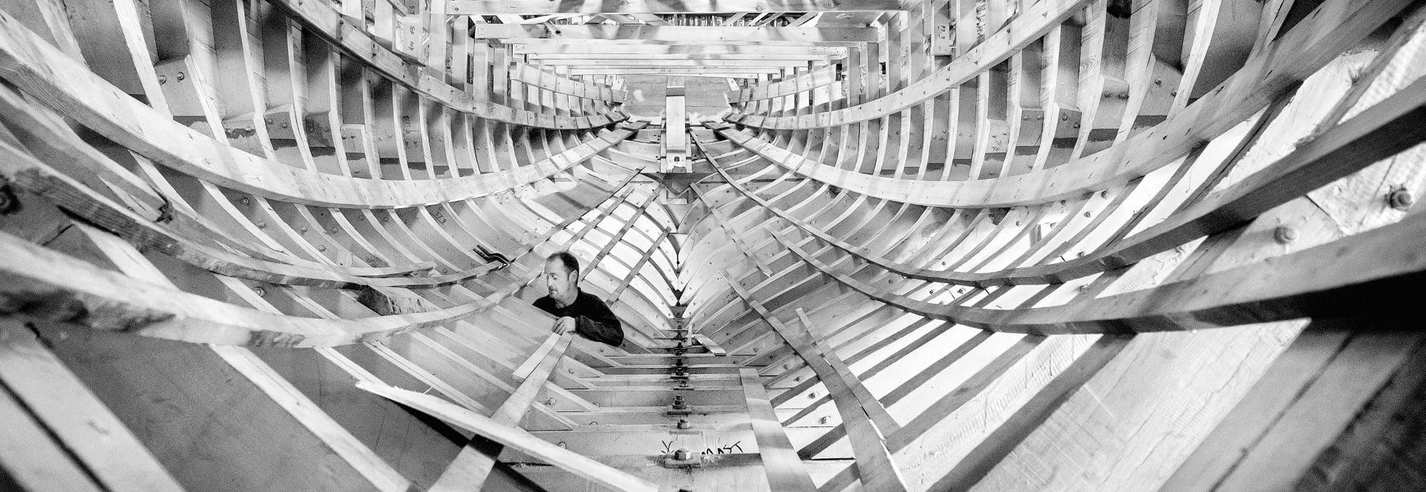 Black and white photo of a man working on a wooden boat.