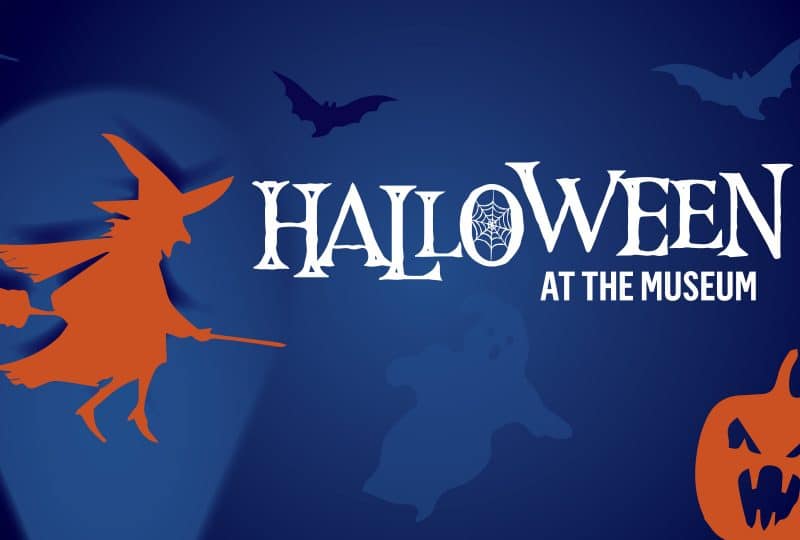 White text reads 'Halloween at the Museum'. The background is a dark blue colour, with orange silhouettes of a witch riding a broom, and a pumpkin with a face carved into it.