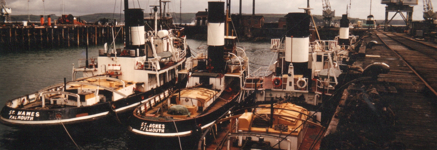 Photo of three Falmouth tugs named 'St Mawes', 'St Agnes' and 'St Merryn' moored side-by-side at a wharf in Falmouth Docks.
