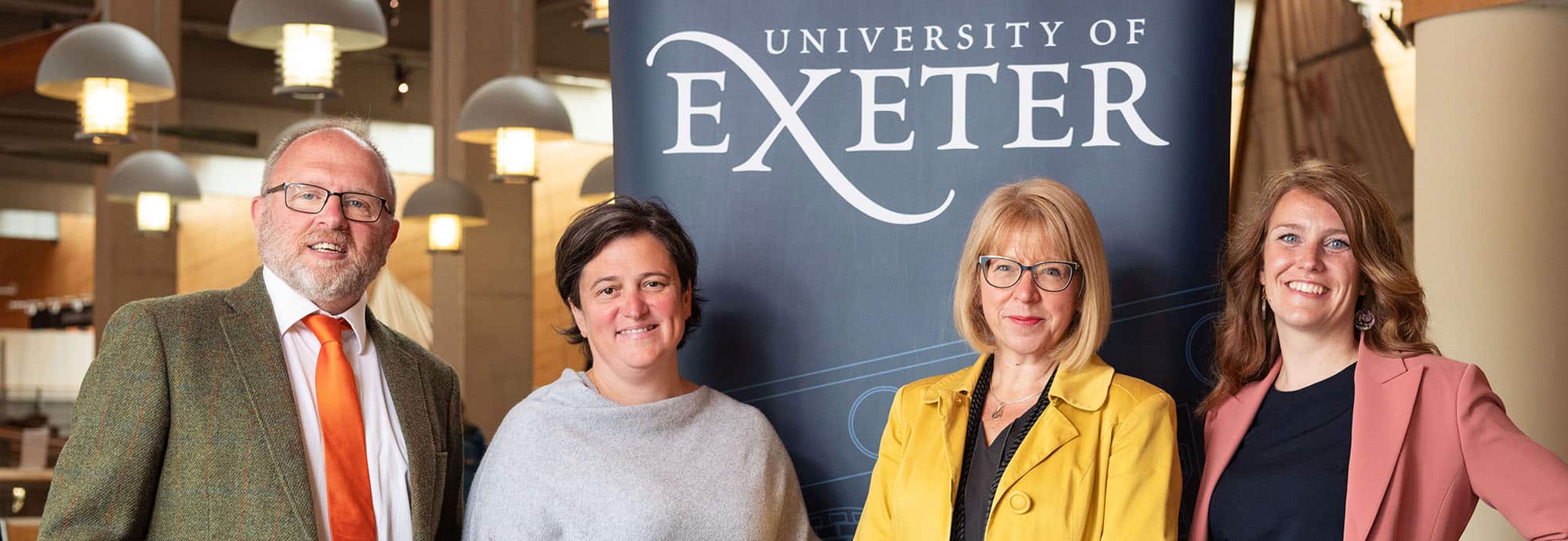 Three women and one man line up for a photo in front of a 'University of Exeter' banner.