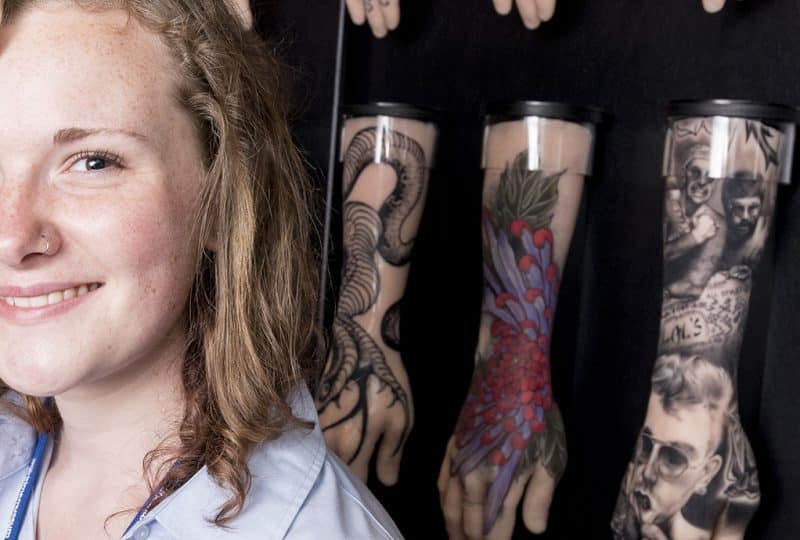 Image of a female volunteer against a wall of tattooed silicone hands.