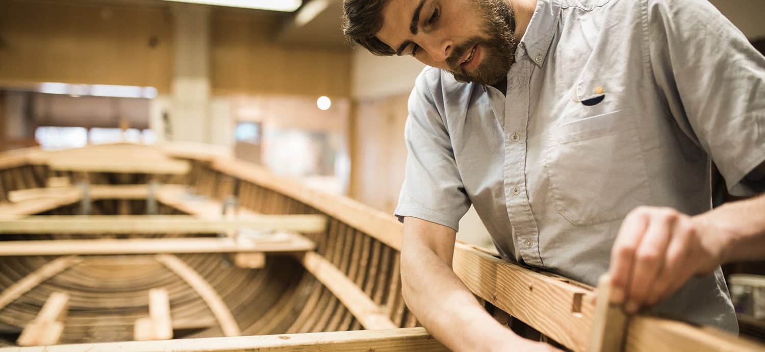 A man works on a wooden boat in a workshop.