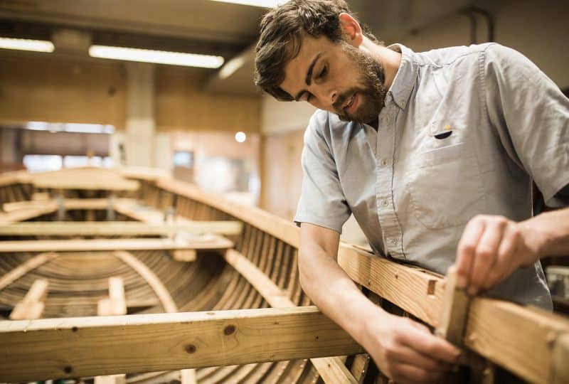 A man works on a wooden boat in a workshop.