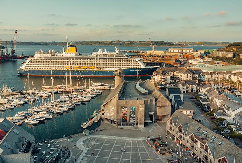 An aerial shot of the museum against Falmouth harbour and the docks. A large cruise ship is moored in one of the berths at the docks.