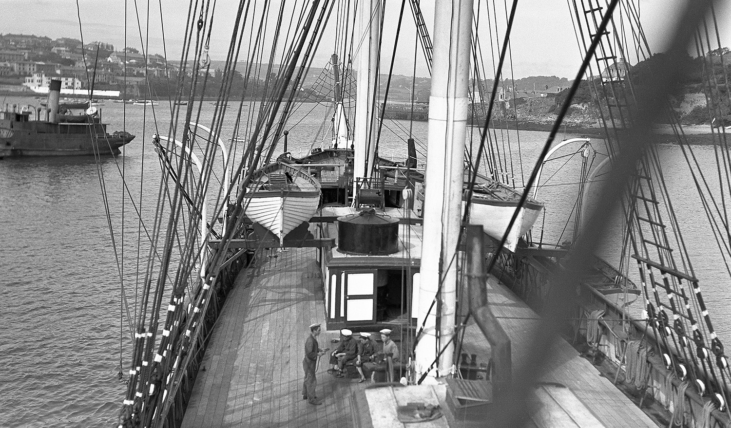 A black and white photo of the deck of the Cutty Sark. Four sailors are sat down on it.