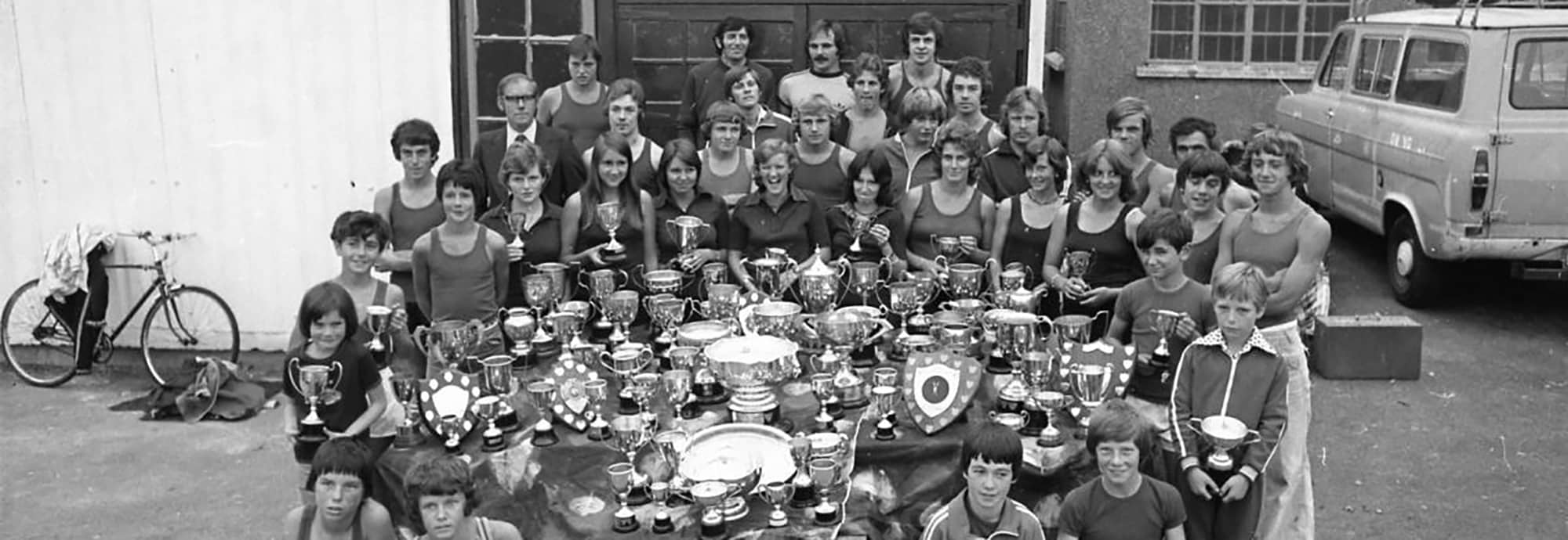 A black and white photograph of the members of Penryn Rowing Club with an array of trophies they have won.