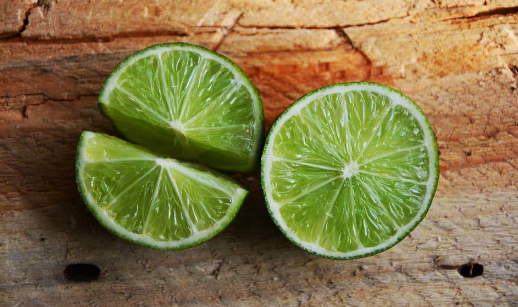 An image of two limes that have been cut in half, resting on a wooden surface.
