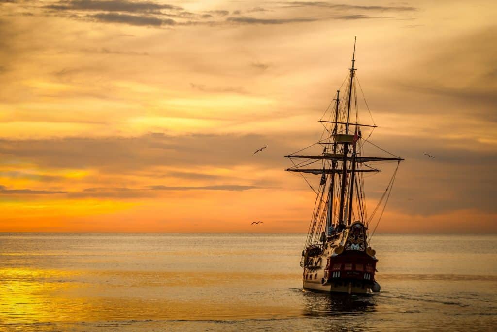 A sailing ship sails into the sunset on calm seas.