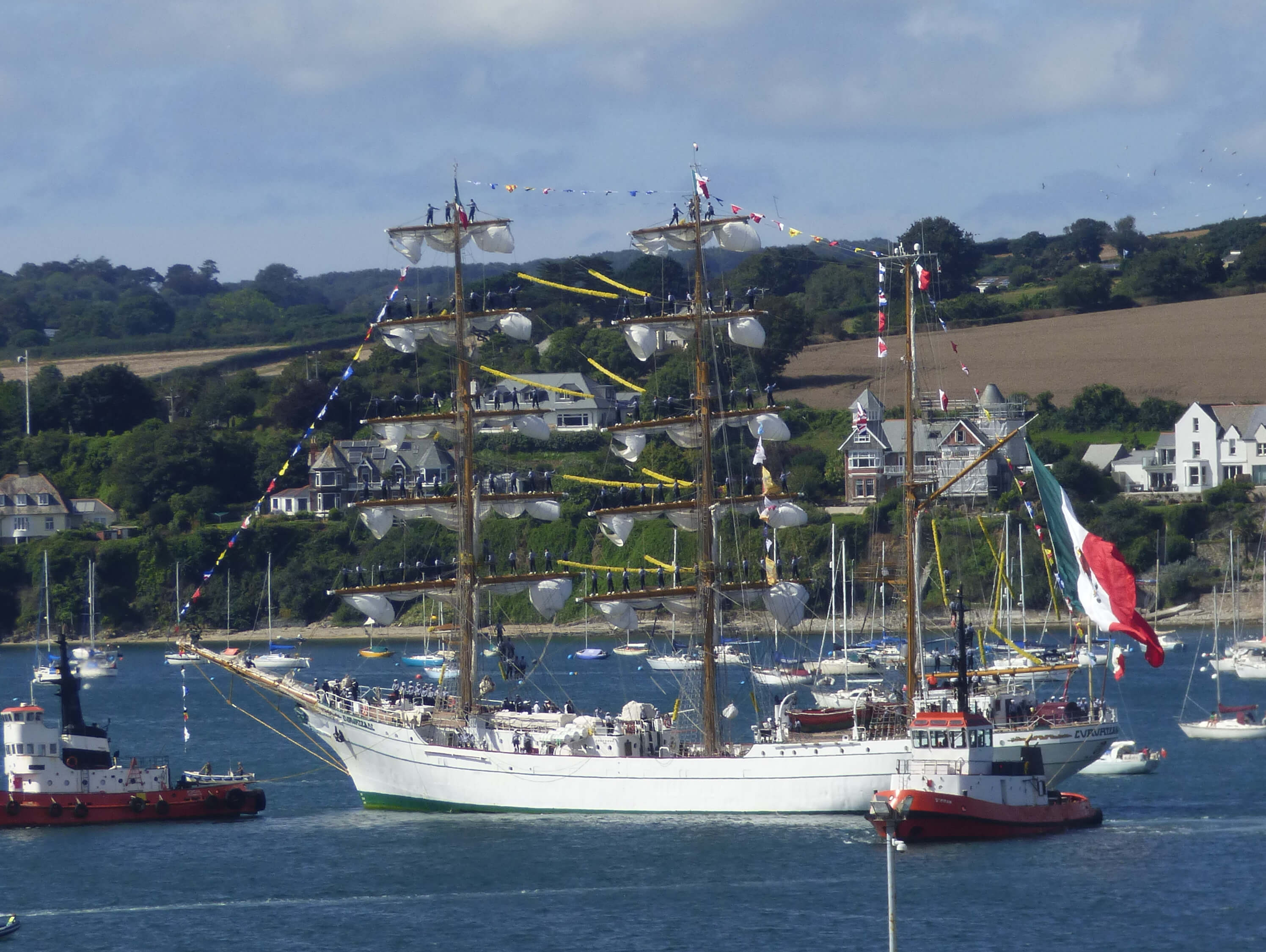 A photo of the Mexican Tall Ship Cuauhtémoc arriving in Falmouth with the crew manning the yards. The photo shows the impressive sight of the ship's crew standing on the yards as the ship sails in.