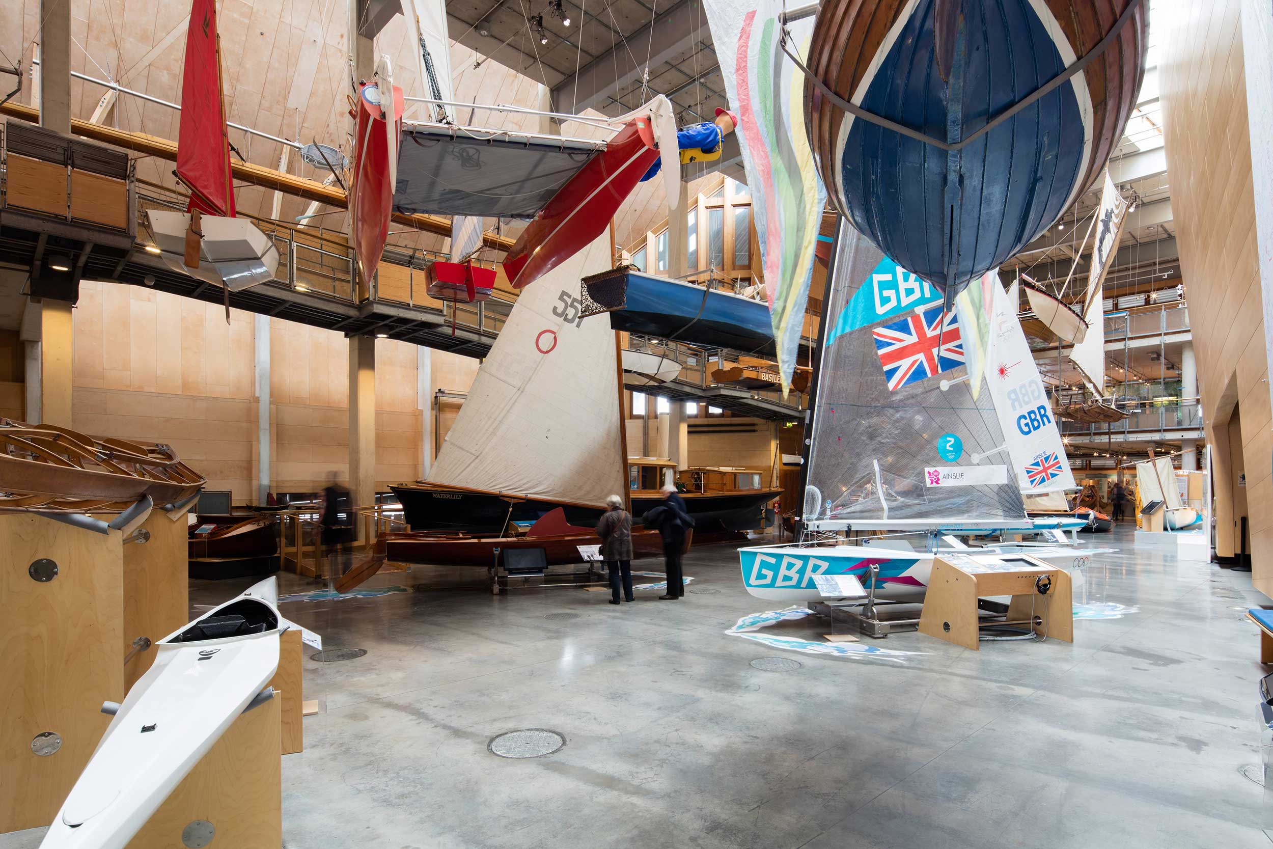 A photo of the Boat Hall at National Maritime Museum Cornwall. Some boats hang from the ceiling, others are positioned on the ground.