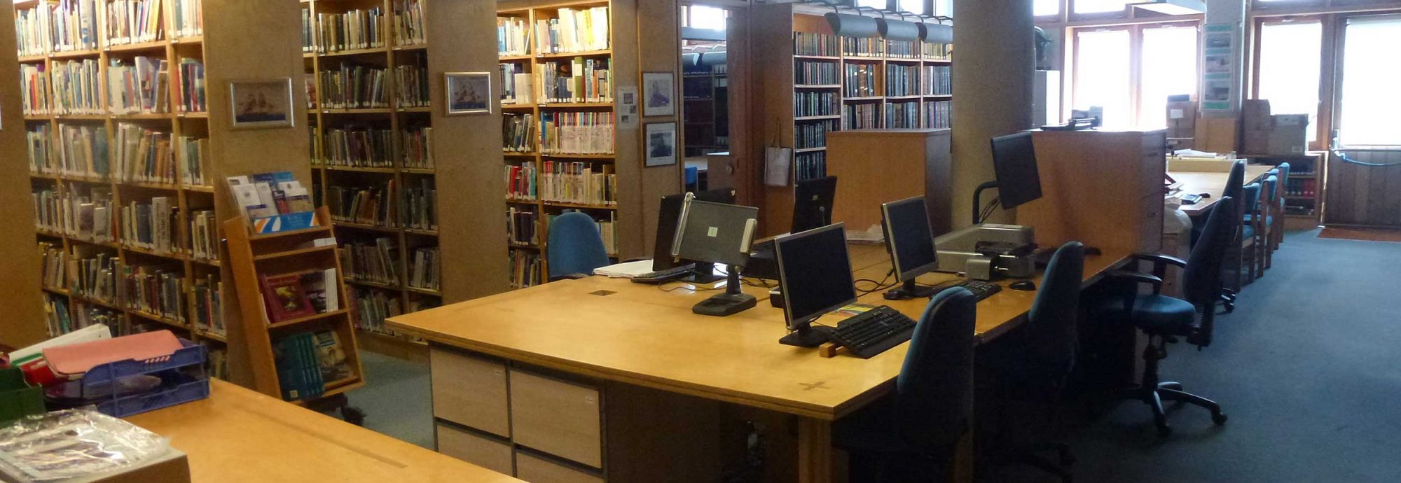 A photo of the Bartlett Library at the Museum. A table in the middle has five computers on it, with rows of books behind it.