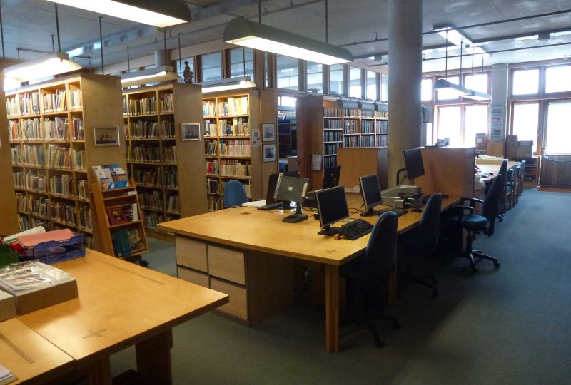 A photo of the Bartlett Library at the Museum. A table in the middle has five computers on it, with rows of books behind it.