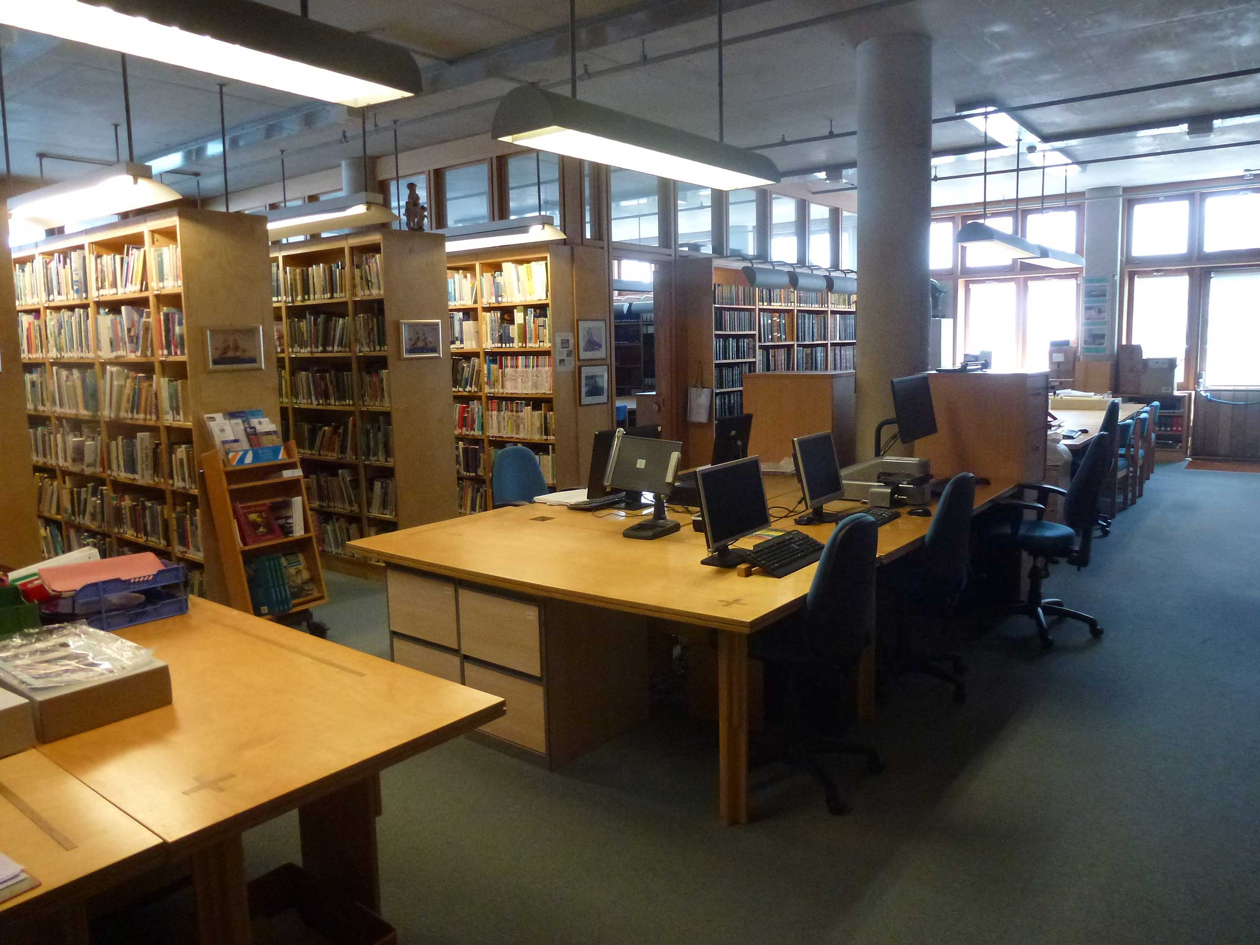 A photo of the Bartlett Library at the Museum. A table in the middle has a handful of computers, with rows of books behind it.
