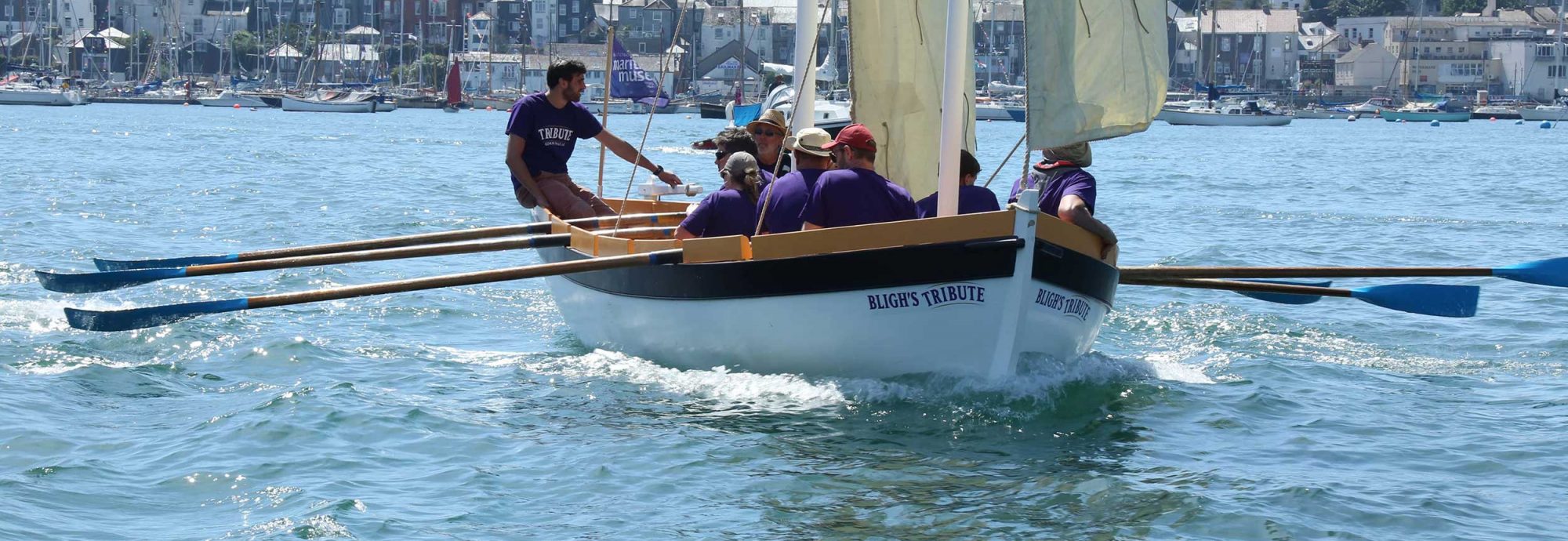 Photo of the 'Bligh's Tribute' boat, with its oars extended, making its way across Falmouth harbour.