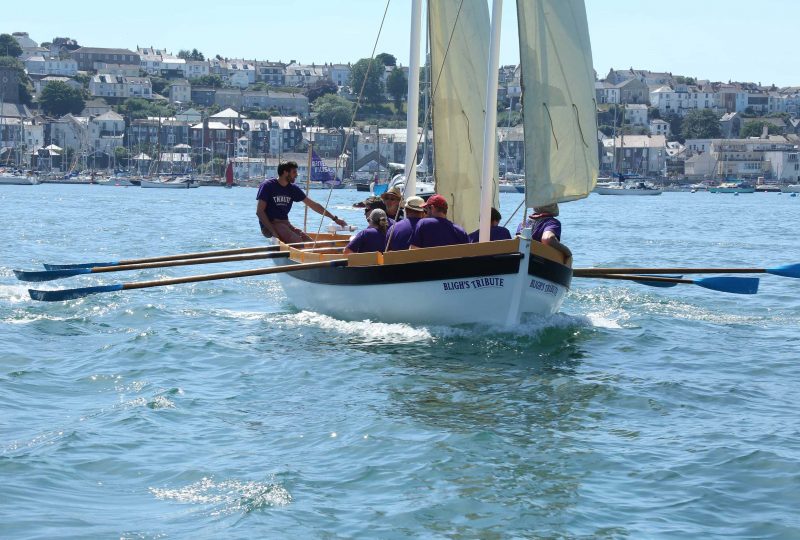 Photo of the 'Bligh's Tribute' boat, with its oars extended, making its way across Falmouth harbour.