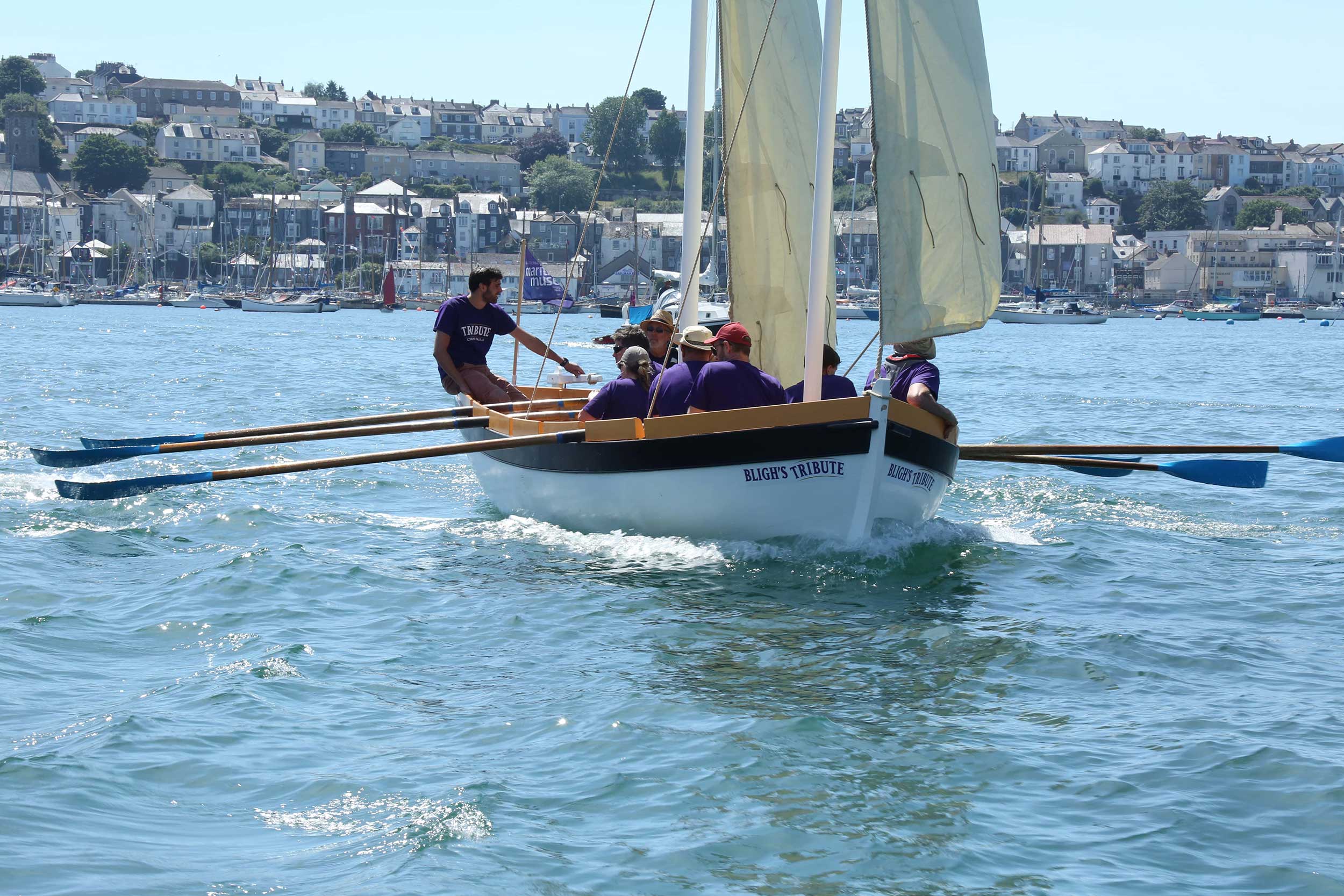 Photo of the 'Bligh's Tribute' boat, with its oars extended, making its way across Falmouth harbour.