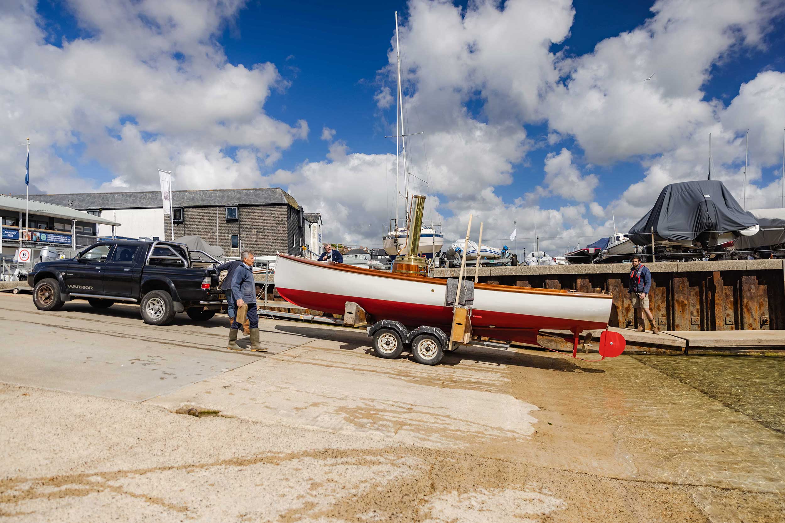 The steam launch 'Emma' is wheeled down a slipway by a 4X4 while on a trailer.