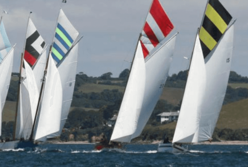 A photo of a group of eight racing boats with coloured topsails.