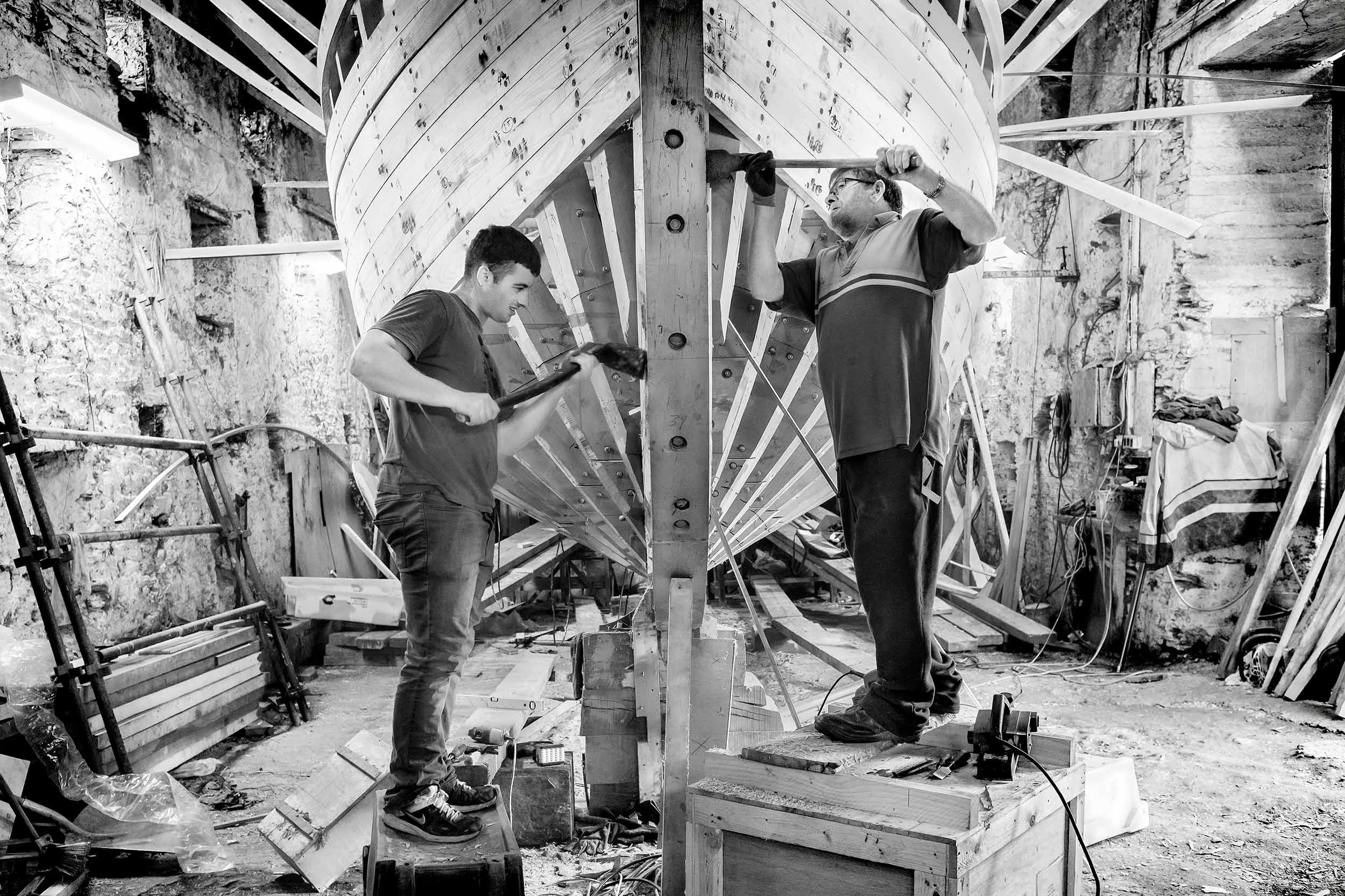 Black and white photo of two men working on a wooden boat.