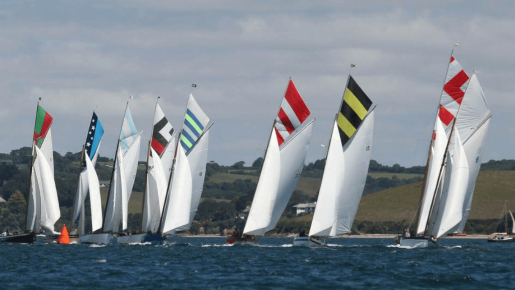 A photo of a group of eight racing boats with coloured topsails.