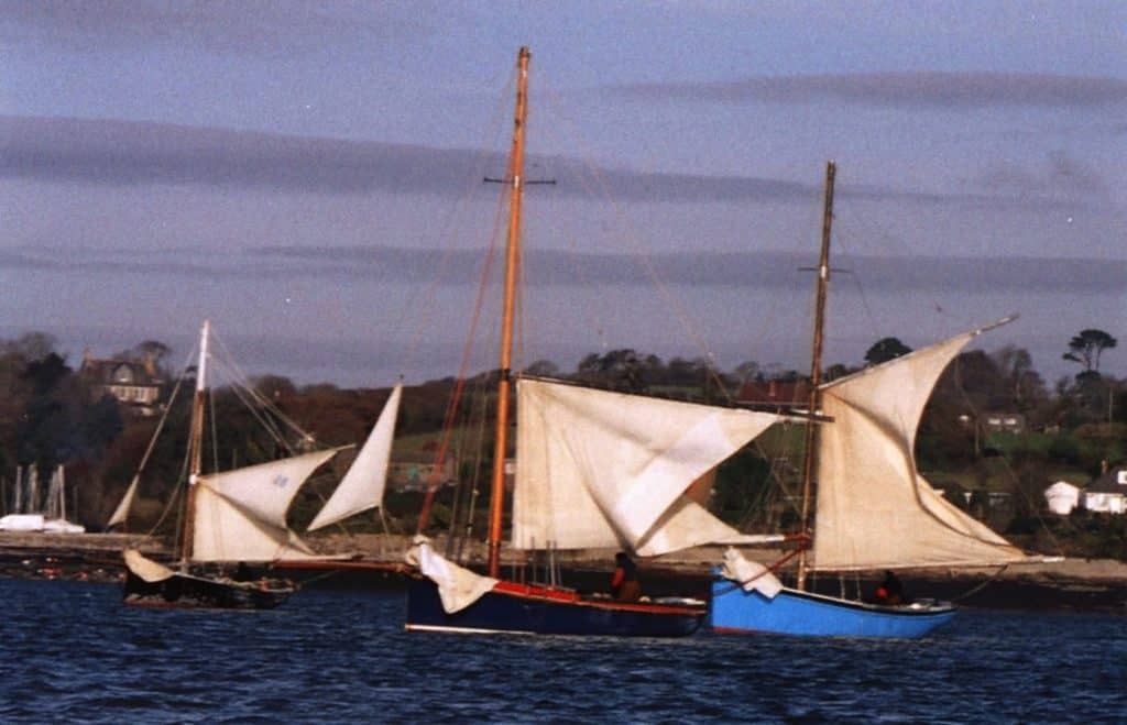 A photo of three boats that formed part of the oyster fleet, named Shadow, Boy Willie, and Six Brothers. Pictured while dredging off Loe Beach with 'scandalised' main sails. 