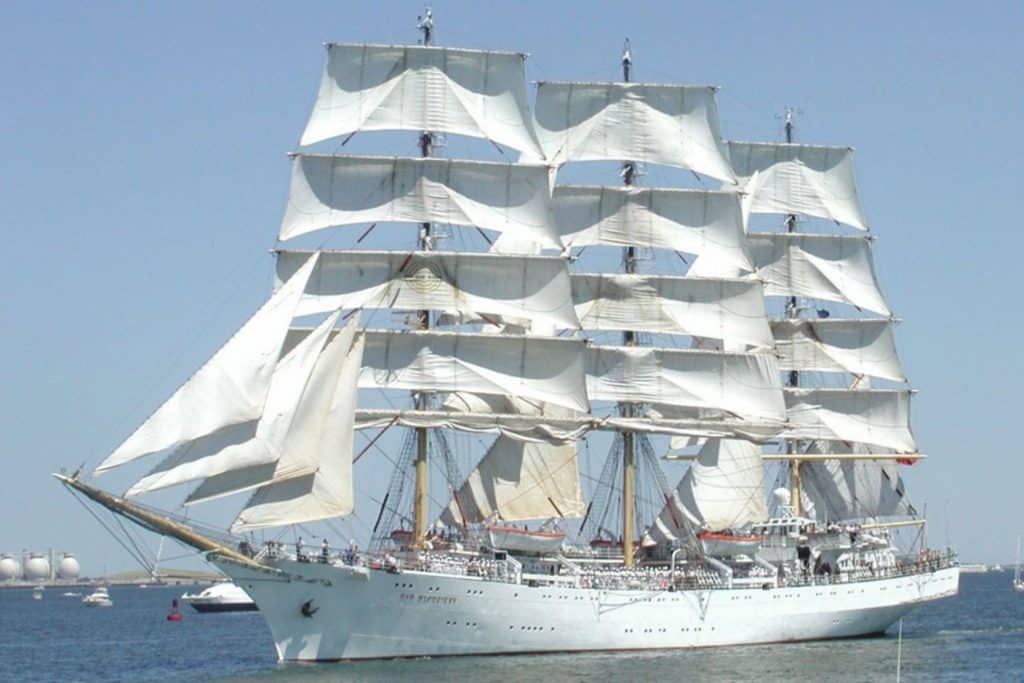 A photo of the Polish Tall Ship Dar Mlodziezy at sea. A large white three-masted sailing ship pictured on a sunny day.
