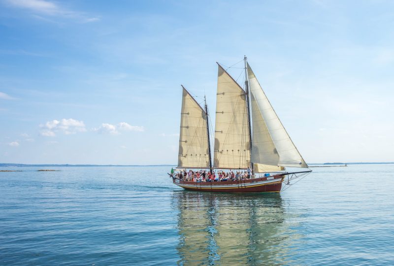 A photo of a sailing ship with white sails sailing on a flat blue ocean.