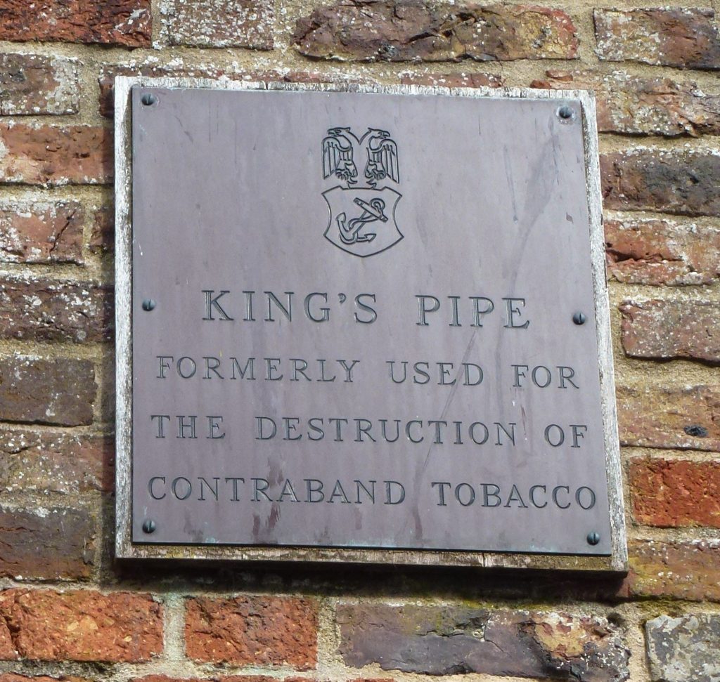A photo of the The King’s Pipe plaque, Custom House Quay, Falmouth. It says: "King's Pipe, formerly used for the destruction of contraband tobacco."