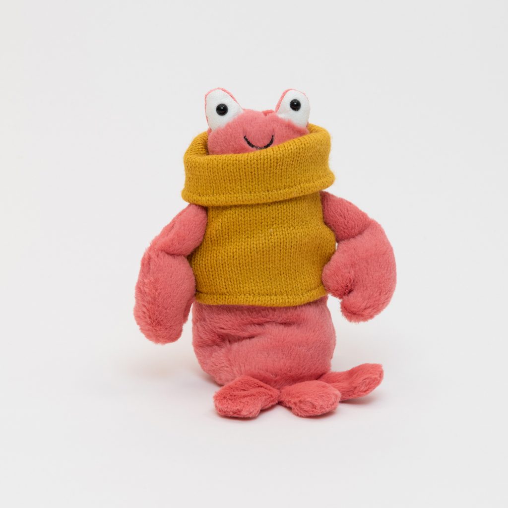 A pink lobster plush toy wearing a mustard-yellow jumper. Pictured on a plain white background.