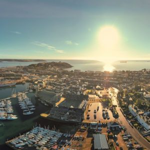 An aerial drone photo of Falmouth overlooking the harbour, National Maritime Museum, and across to Pendennis Headland and out to sea. The photo is taken on a sunny day.