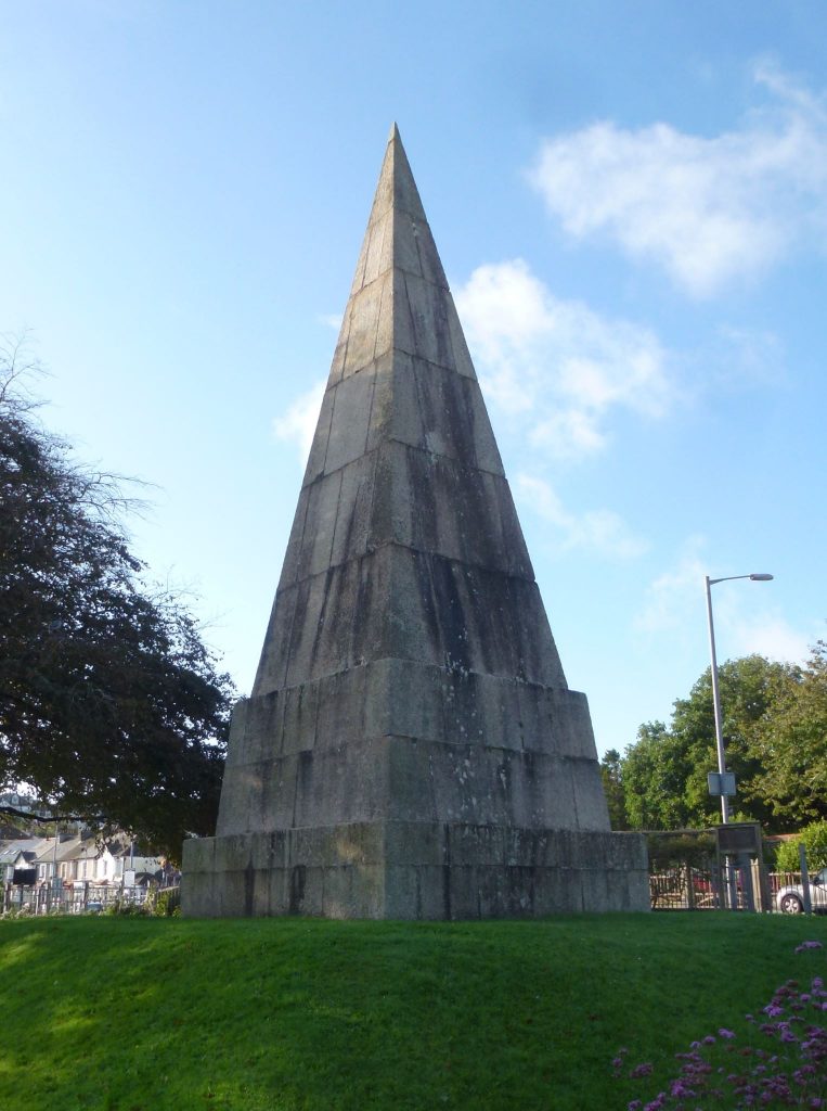A photo of the Killigrew Monument, Grove Place, Falmouth. Its tall, grey pyramid shape is pictured on a sunny day.